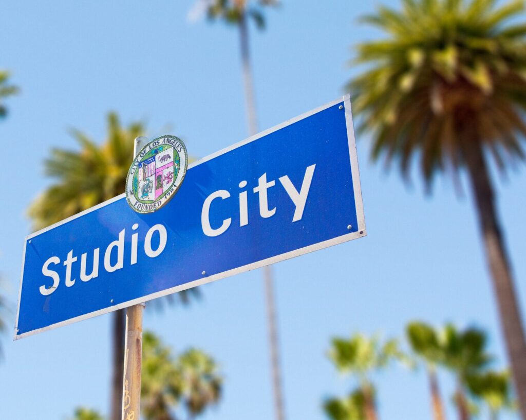 Studio City street sign with palm trees in the background under a clear blue sky.