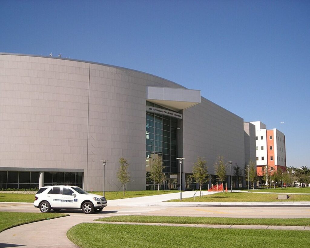Modern Frost Art Museum building with curved architecture, glass entrance, and landscaped grounds under a clear blue sky.