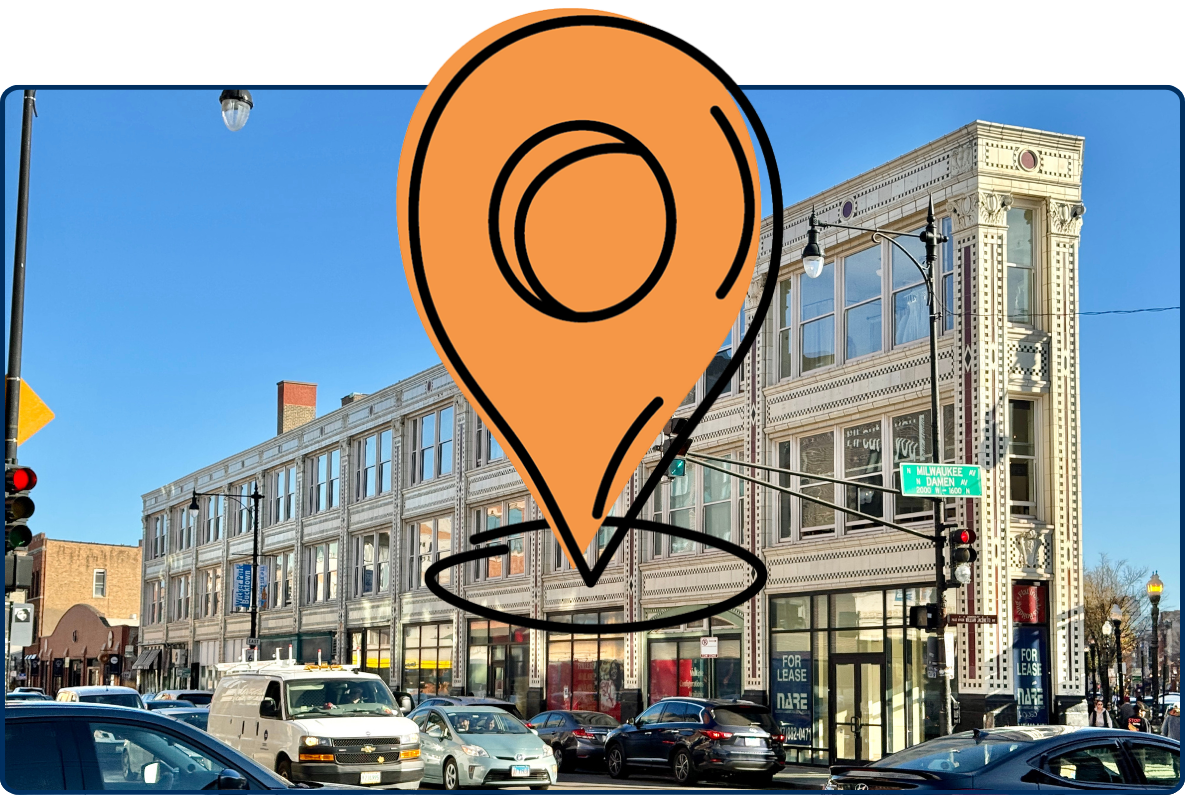 Street-level view of the historic Flatiron Arts Building in Chicago’s Wicker Park neighborhood, featuring the distinctive wedge-shaped terra-cotta building at the intersection of Milwaukee Avenue and North Avenue, with large storefront windows, decorative architectural details, pedestrians, and city traffic under a clear sky.