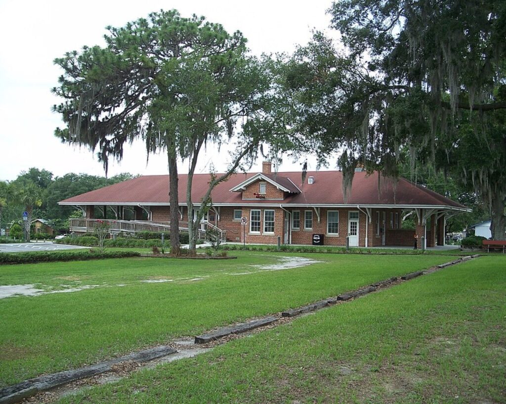 Zephyrhills Depot Museum building with a red roof, large oak trees, and grassy grounds in Zephyrhills, Florida.