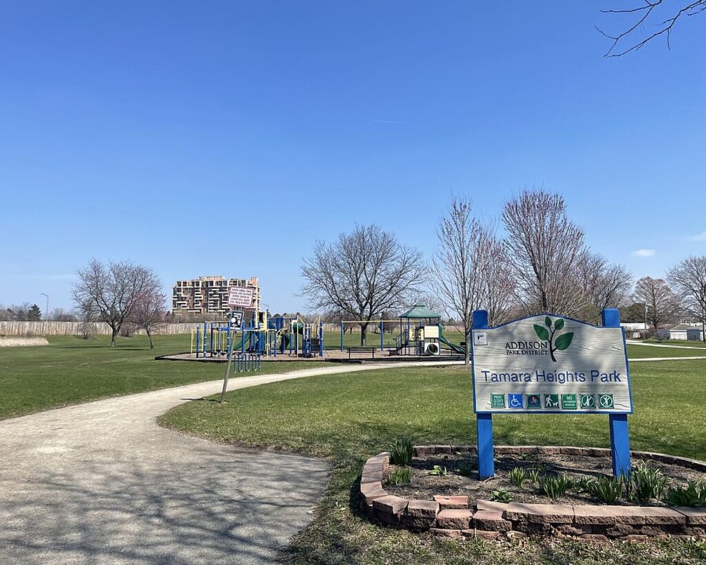 Tamara Heights Park in Addison, Illinois with playground, walking path, park sign, and clear blue sky.