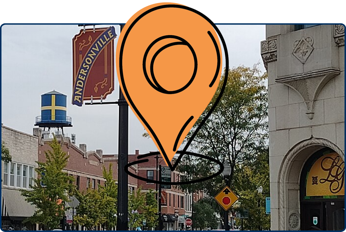 Andersonville street scene with storefronts, parked cars, sidewalk planters, a neighborhood banner, and a water tower in the background.