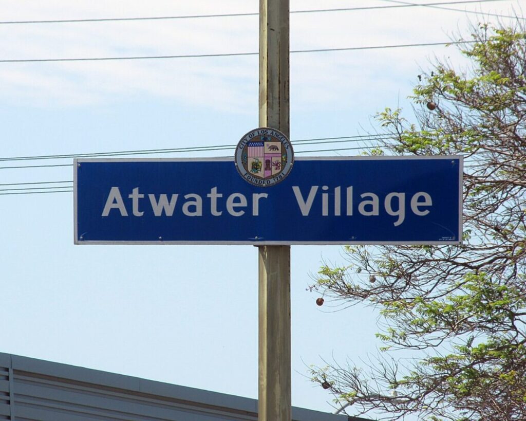 Atwater Village neighborhood sign on a pole with power lines, trees, and clear sky.
