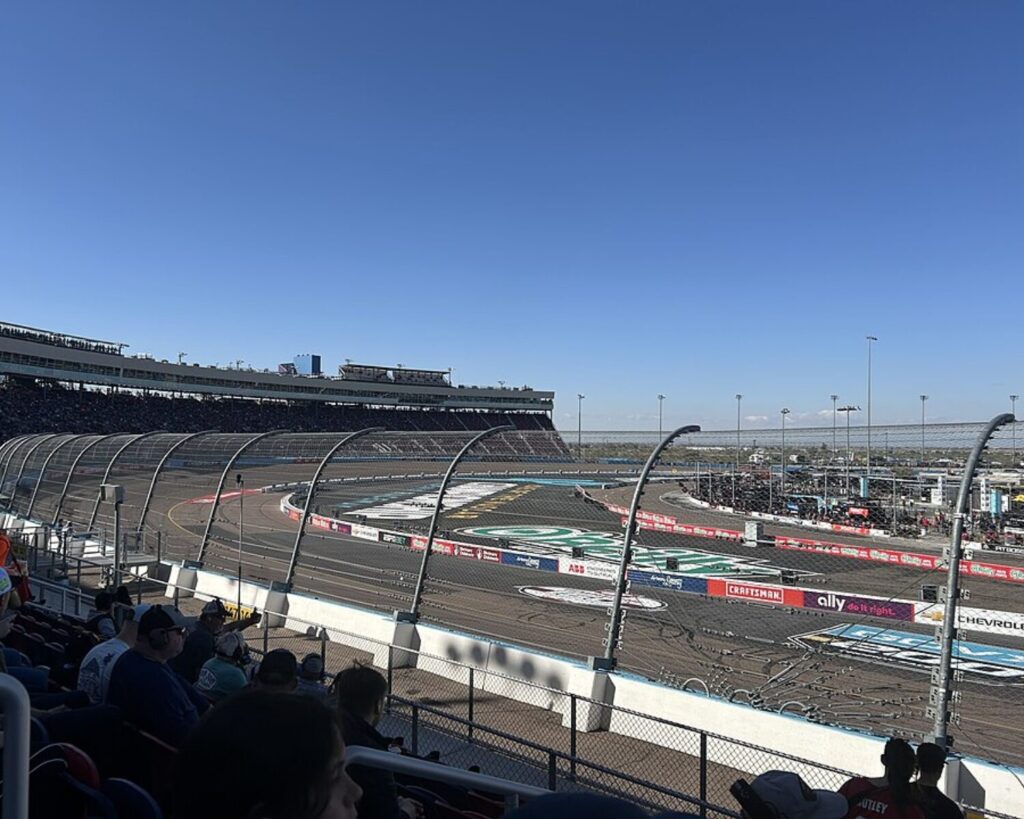 Phoenix Raceway with race track, grandstands, spectators, and clear blue sky.