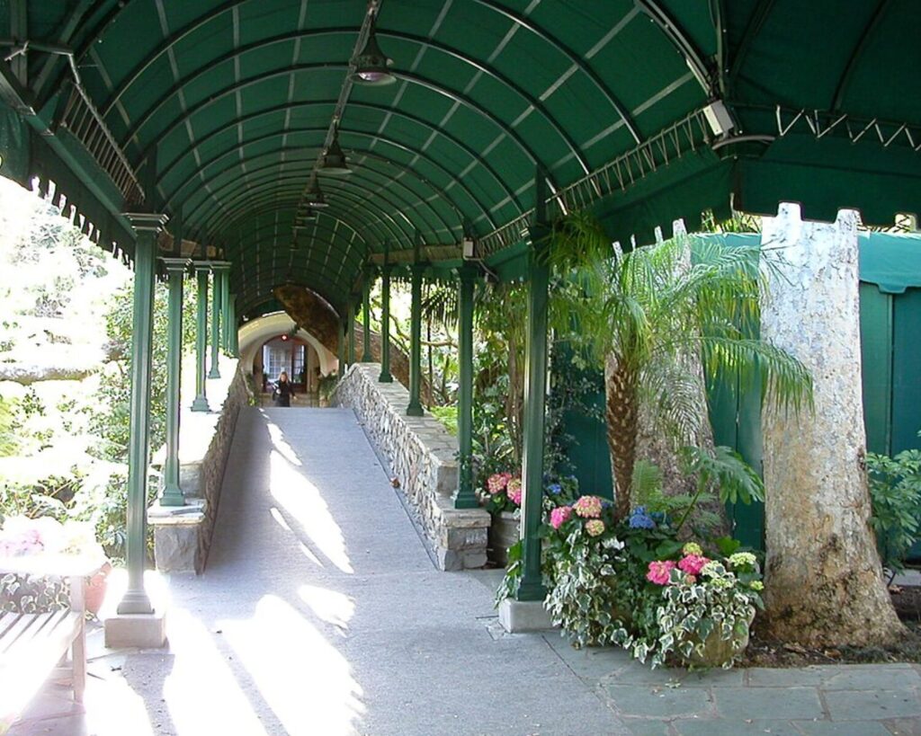 Hotel Bel-Air entrance walkway with green canopy, stone walls, plants, and flowers.