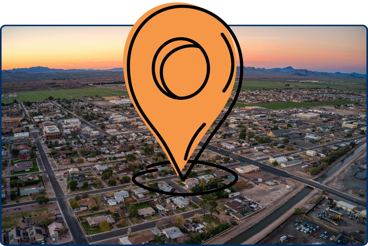 Aerial view of Buckeye, Arizona at sunrise with suburban homes, roads, farmland, and mountains in the distance.