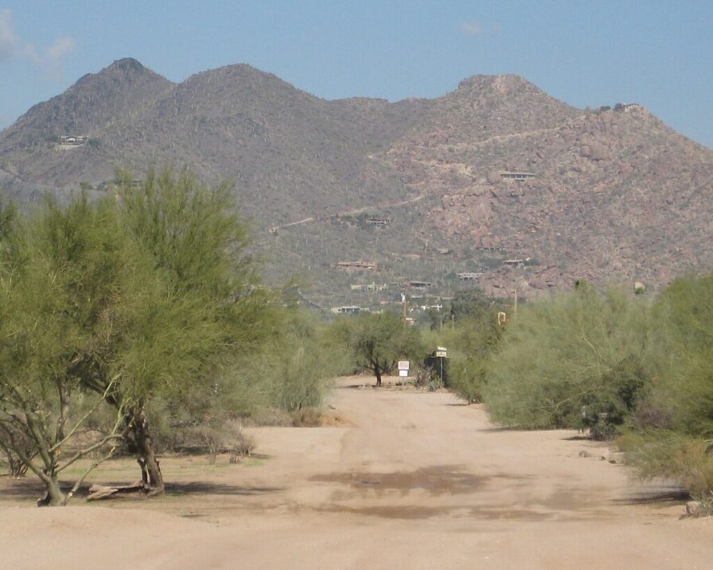 Black Mountain near Cave Creek, Arizona with a sandy desert road, green shrubs, and rocky hills under a clear sky.