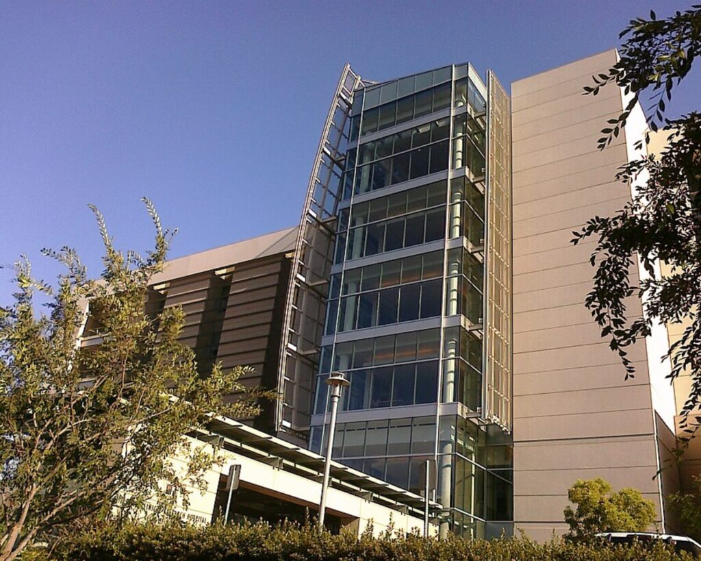 Helford Hospital at City of Hope with modern glass building, trees, and clear blue sky.