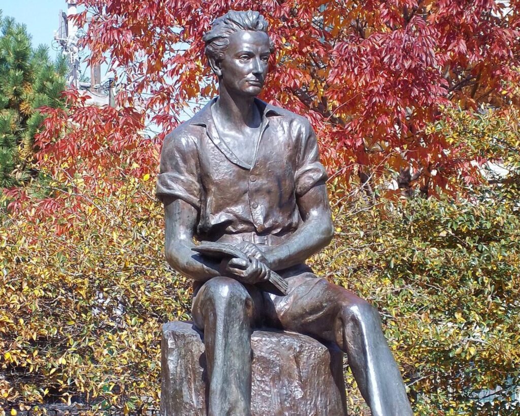Bronze statue of young Lincoln seated on a tree stump with autumn-colored trees in the background.