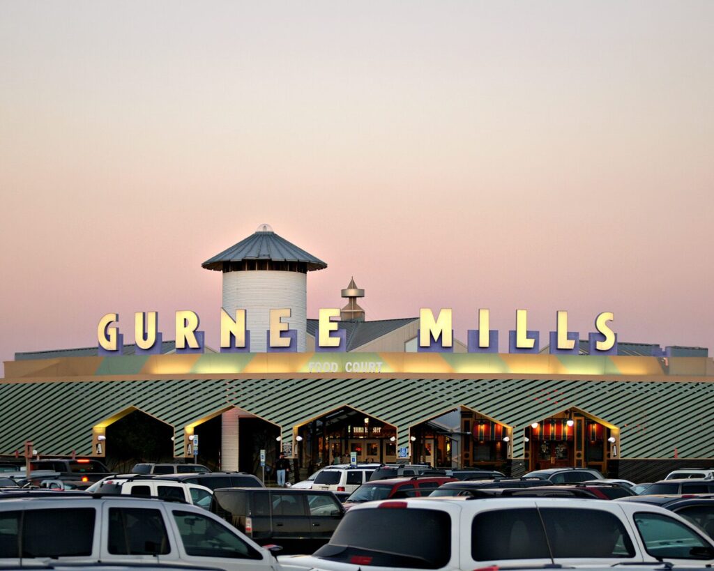 Gurnee Mills mall entrance with large sign, food court, parked cars, and evening sky.
