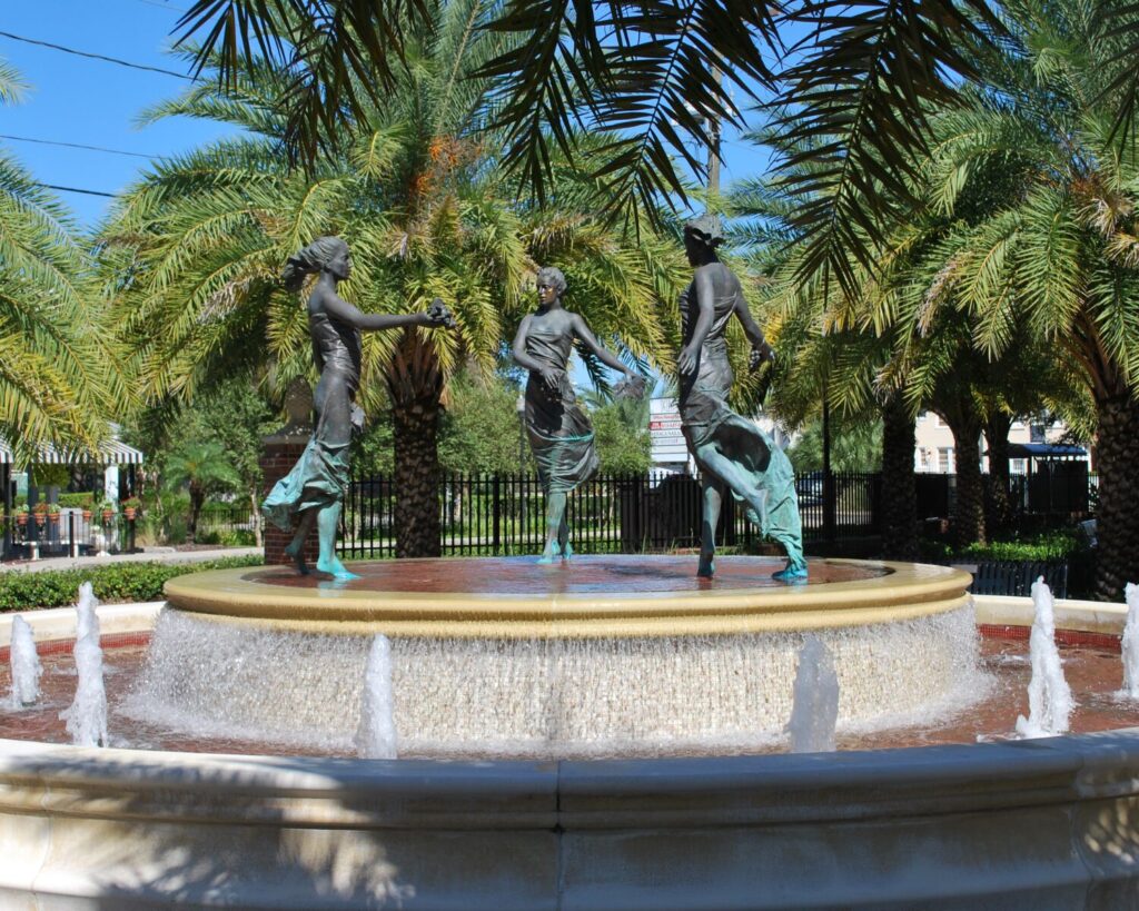 Hyde Park fountain with bronze statues, water jets, palm trees, and clear blue sky.