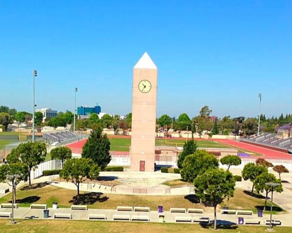 Clock tower on a college campus with a red running track, bleachers, and green lawns on a sunny day