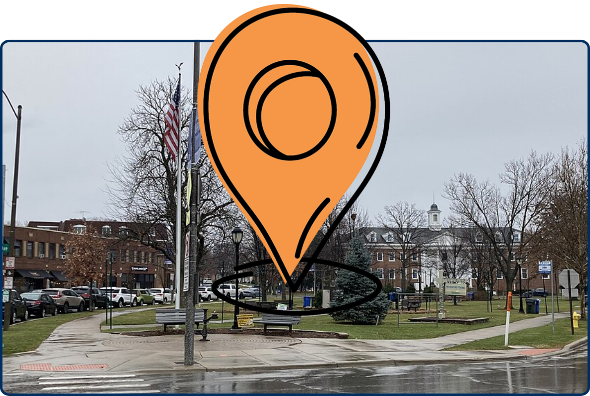 Hodges Park in Park Ridge with sidewalks, benches, flags, leafless trees, and wet streets on a cloudy day.