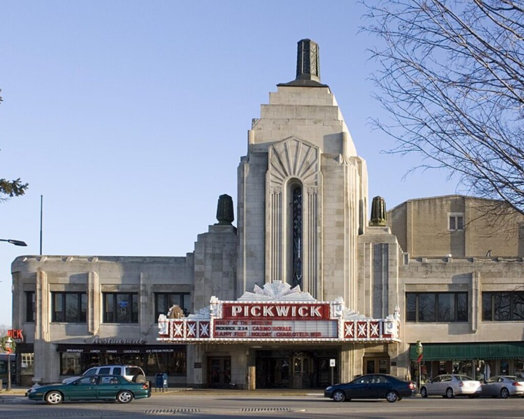 Art Deco Pickwick Theatre façade with a red marquee, along a city street with cars parked in front.