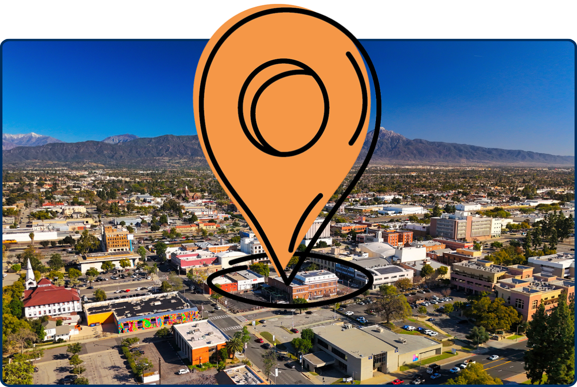 Aerial view of Pomona, California with city buildings and the San Gabriel Mountains under a clear blue sky.