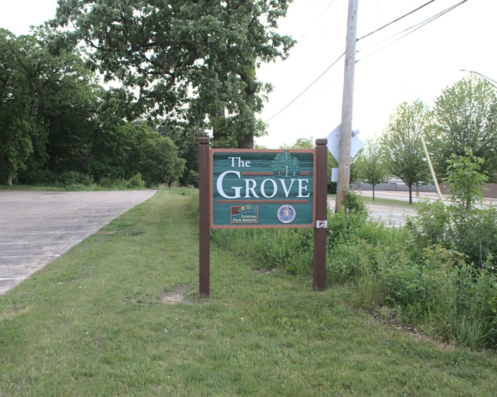 The Grove park sign in Rolling Meadows, Illinois, beside a grassy roadside with trees and greenery.