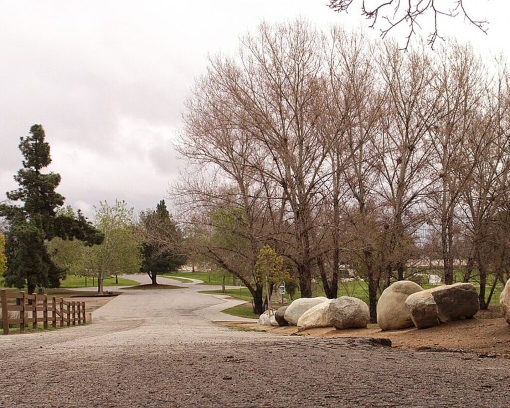 Woodley Park access road with trees, large rocks, grass, and cloudy sky.