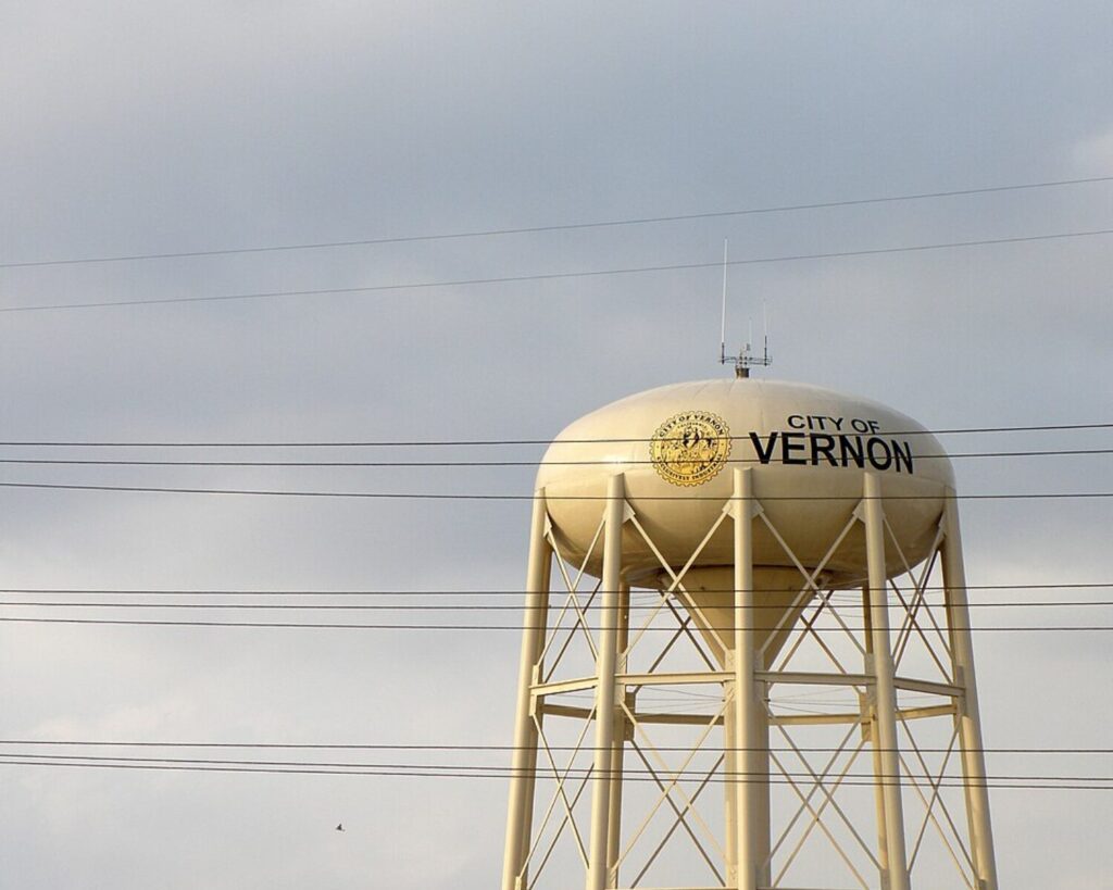 Water tower labeled City of Vernon standing against a cloudy sky with power lines crossing the foreground.
