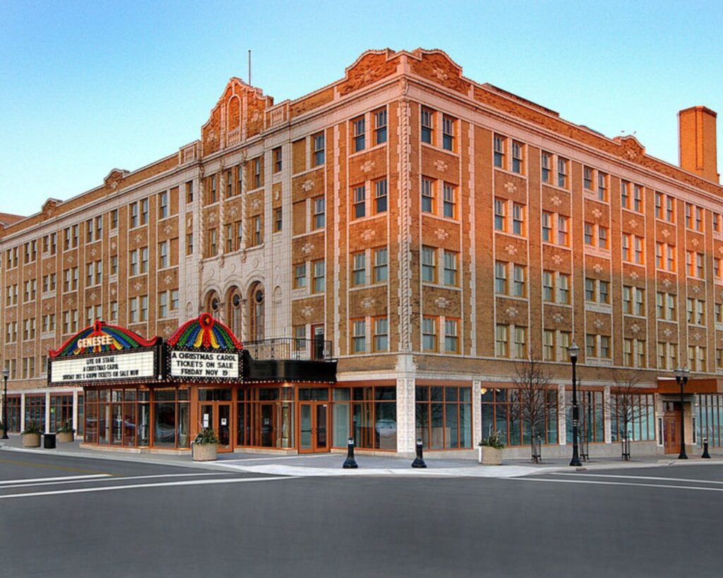 Genesee Theatre exterior with historic brick facade, marquee entrance, empty street, and clear sky.