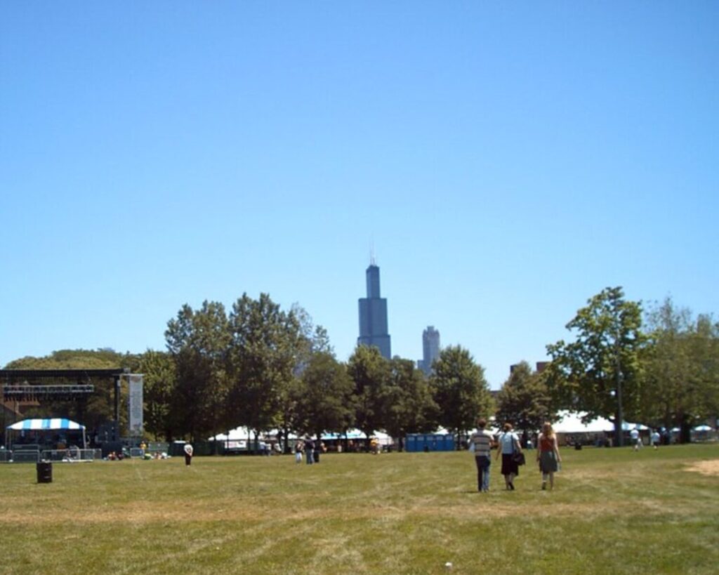 Park with open field, trees, and distant Chicago skyline including the Willis Tower under a clear blue sky.