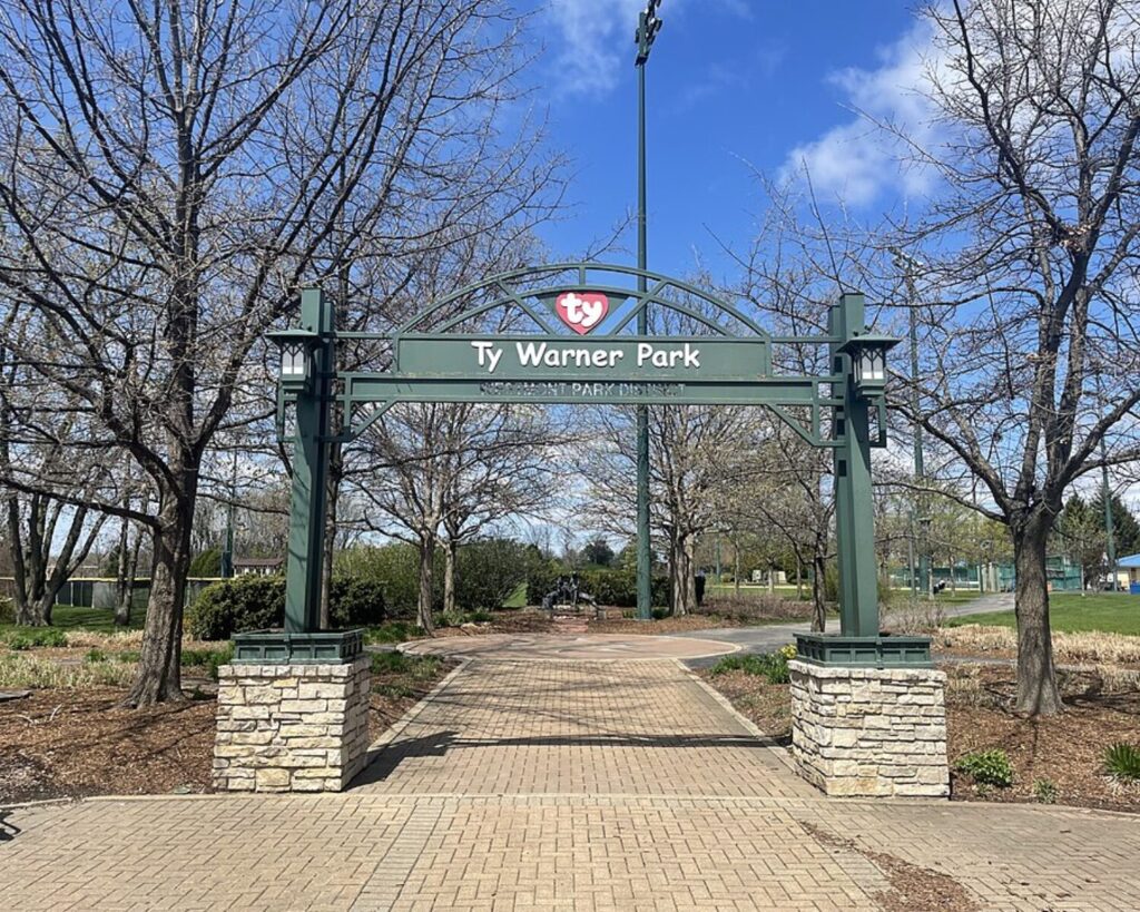 Ty Warner Park entrance arch in DuPage County, Illinois with brick walkway, trees, and blue sky.