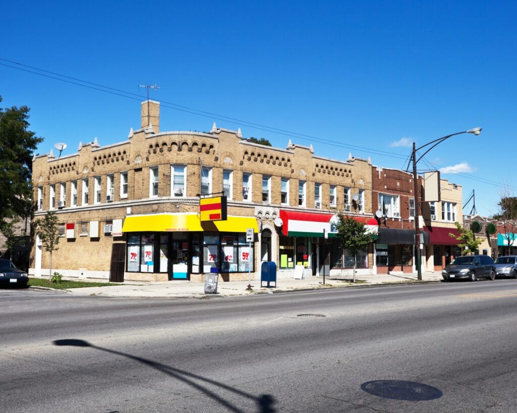 Vintage storefronts beneath brick apartments along a sunny street in Belmont Cragin, Chicago.