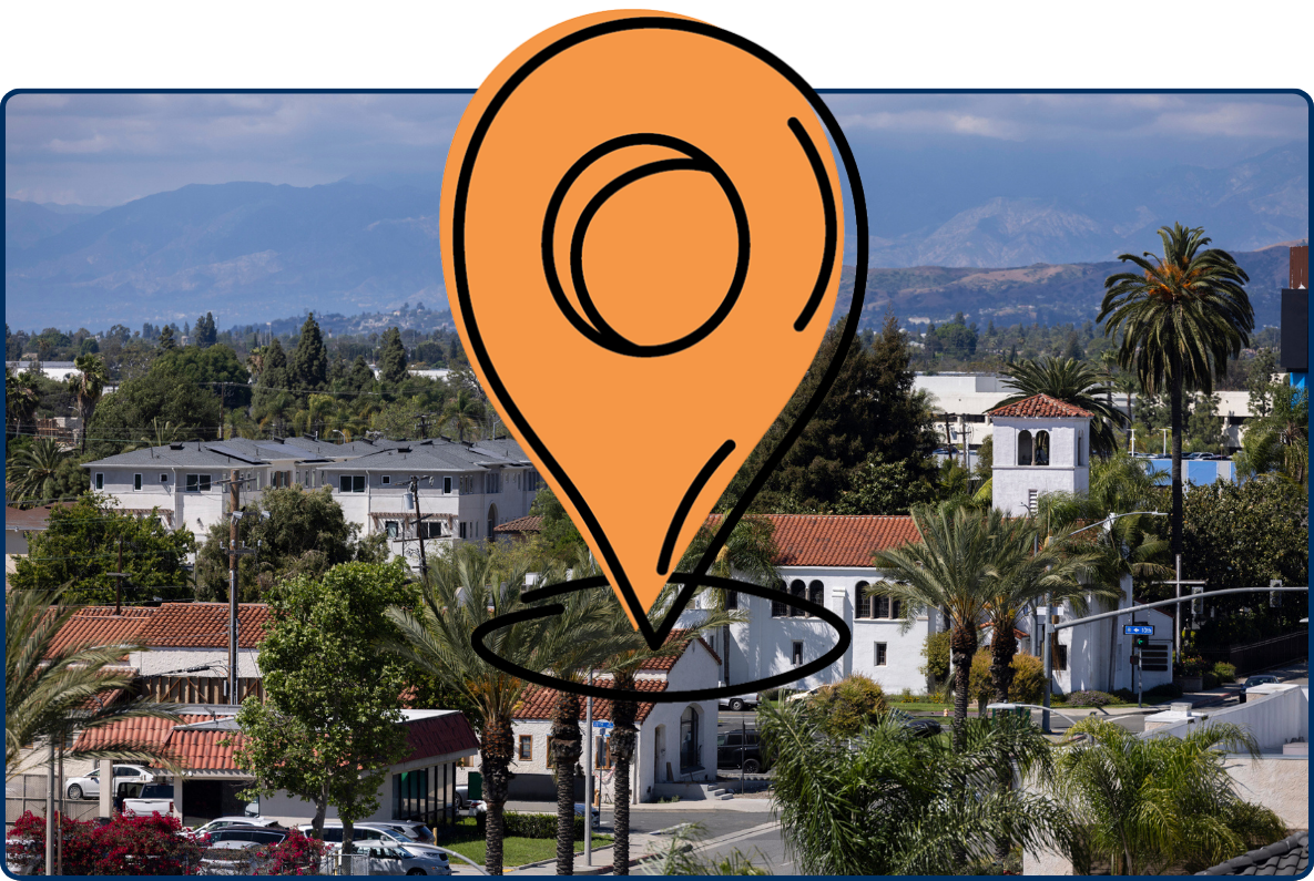 Historic Buena Park, California with palm trees, Spanish-style buildings, rooftops, and mountains in the background.