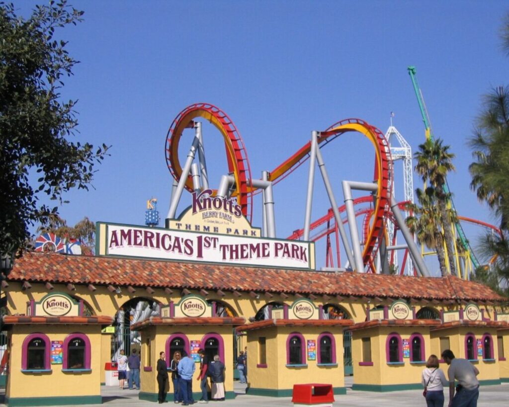 Knott’s Berry Farm entrance with roller coaster tracks, colorful gate, visitors, and clear blue sky.