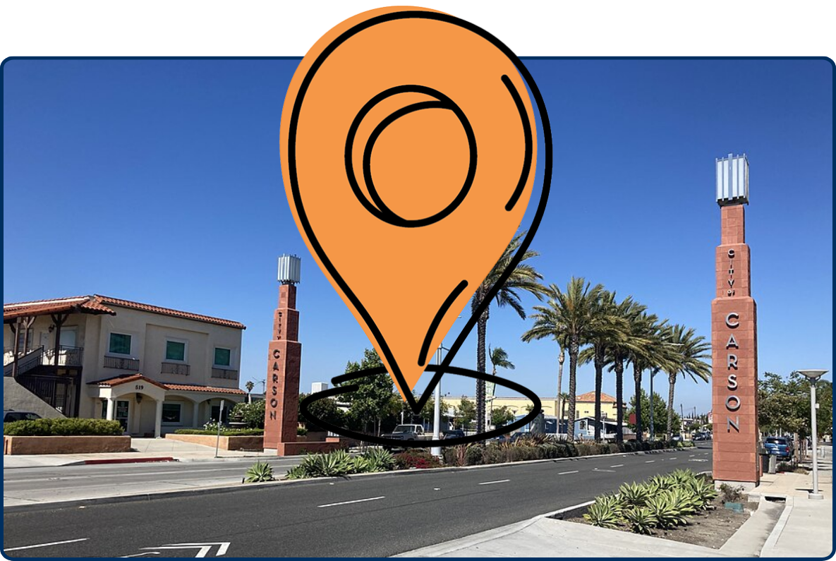 South Bay Los Angeles street in Carson with palm trees, brick gateway towers, sidewalks, and clear blue sky.