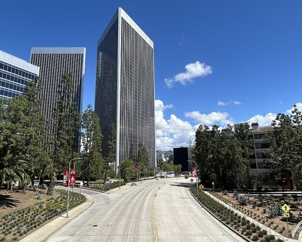 Olympic Boulevard in Century City with tall office towers, tree-lined street, and clear blue sky.