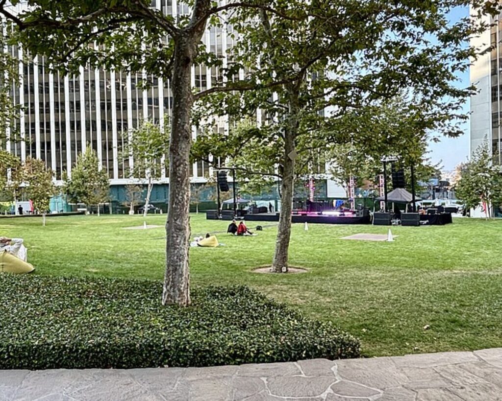 Century Park in Century City with green lawn, trees, people relaxing, and tall office buildings.