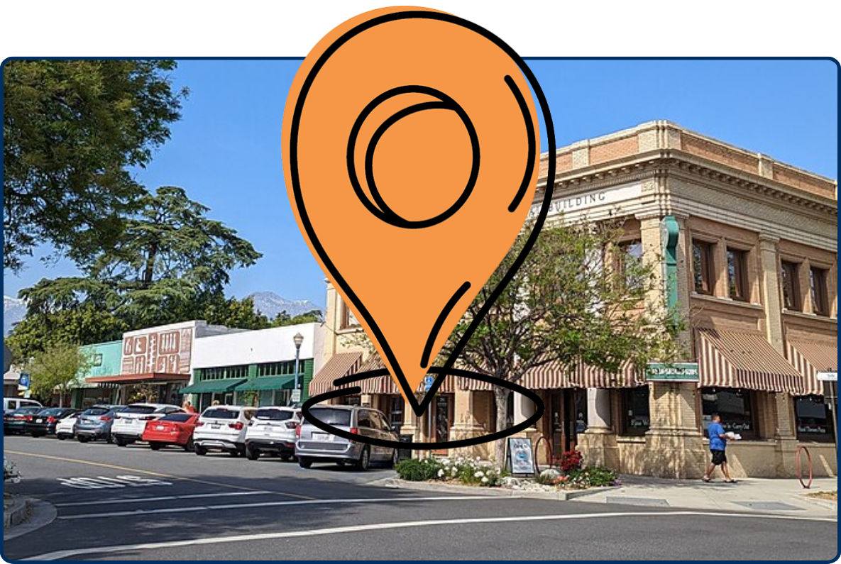 Verbal Building and intersection in Claremont, California, with parked cars, storefronts, trees, and mountains in the background.