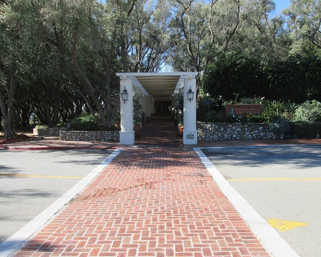 Padua Hills Theatre entrance with brick walkway, white columns, stone walls, trees, and shaded greenery.
