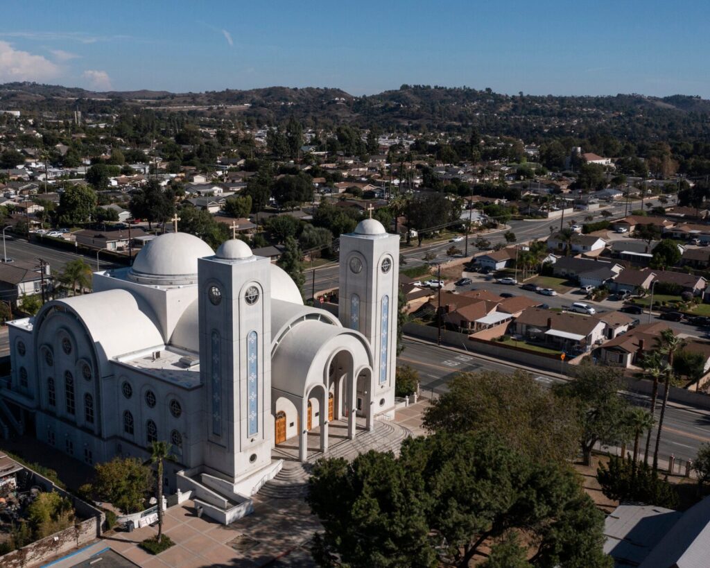 Aerial view of a large white church with multiple domes and twin towers in a residential suburb.