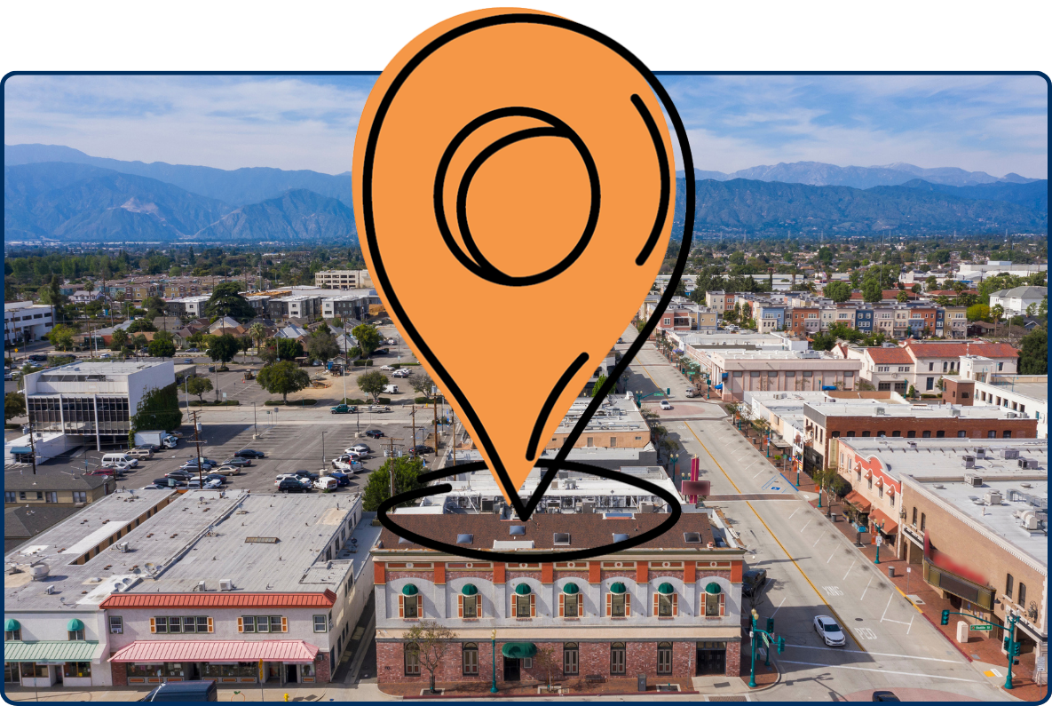 Aerial view of Covina, California with downtown buildings, streets, and mountains in the background.