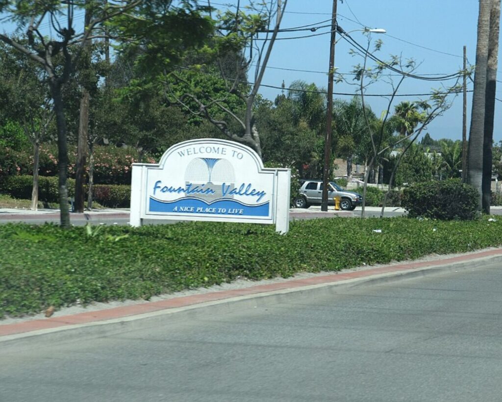 Welcome to Fountain Valley sign with Water Fountain graphic and slogan 'A Nice Place to Live' on a landscaped roadside median.