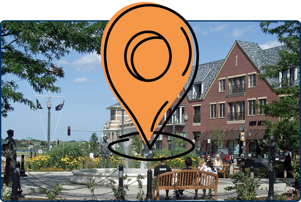 Outdoor plaza at The Glen Town Center with a fountain, sculptures, benches, landscaped flowers, and brick buildings.
