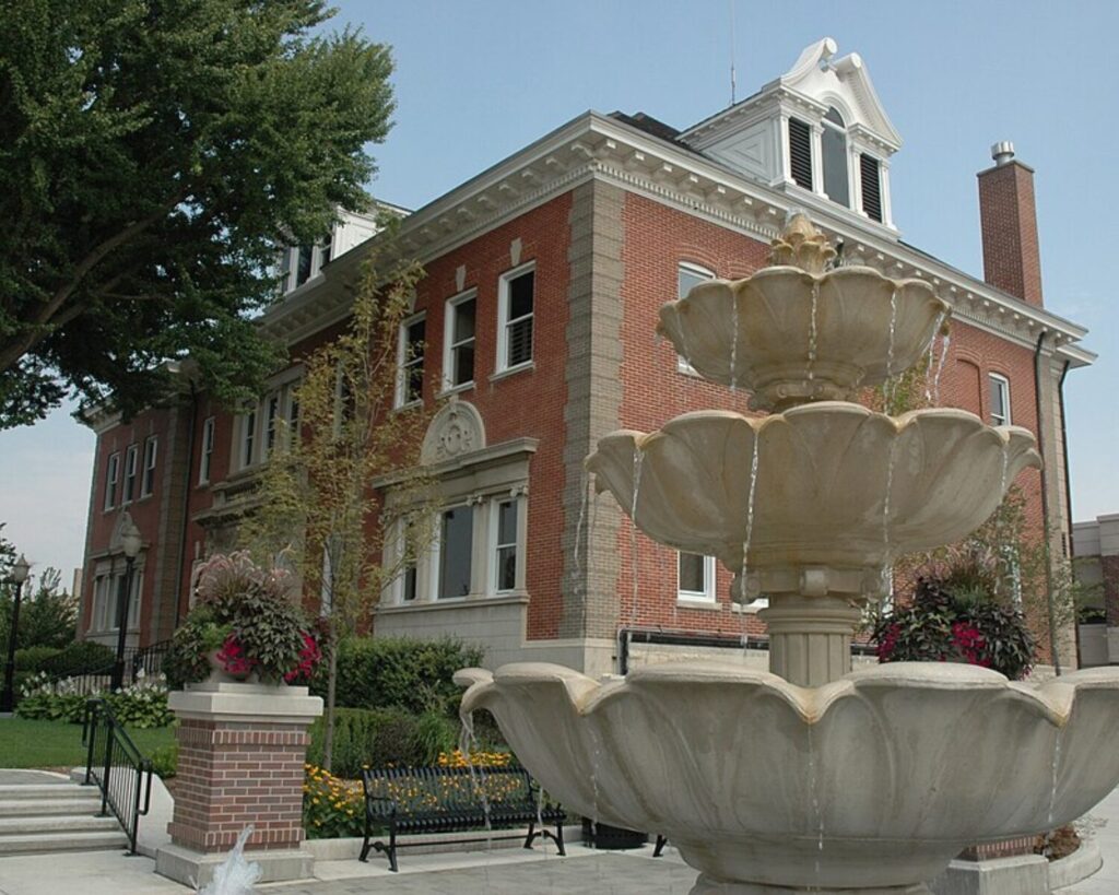 La Grange Village Hall, a historic red-brick civic building with a tiered stone fountain and landscaped grounds in front.