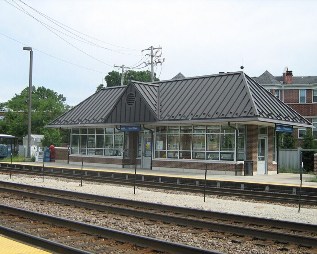 MontClare Metra station with a brick-and-glass depot, metal roof, platform, and railway tracks in the foreground.