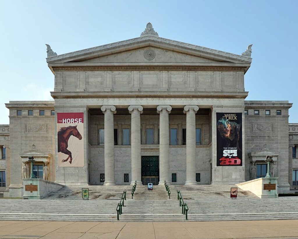 Neoclassical museum facade with six tall columns, wide steps, and exhibition banners on either side of the entrance.