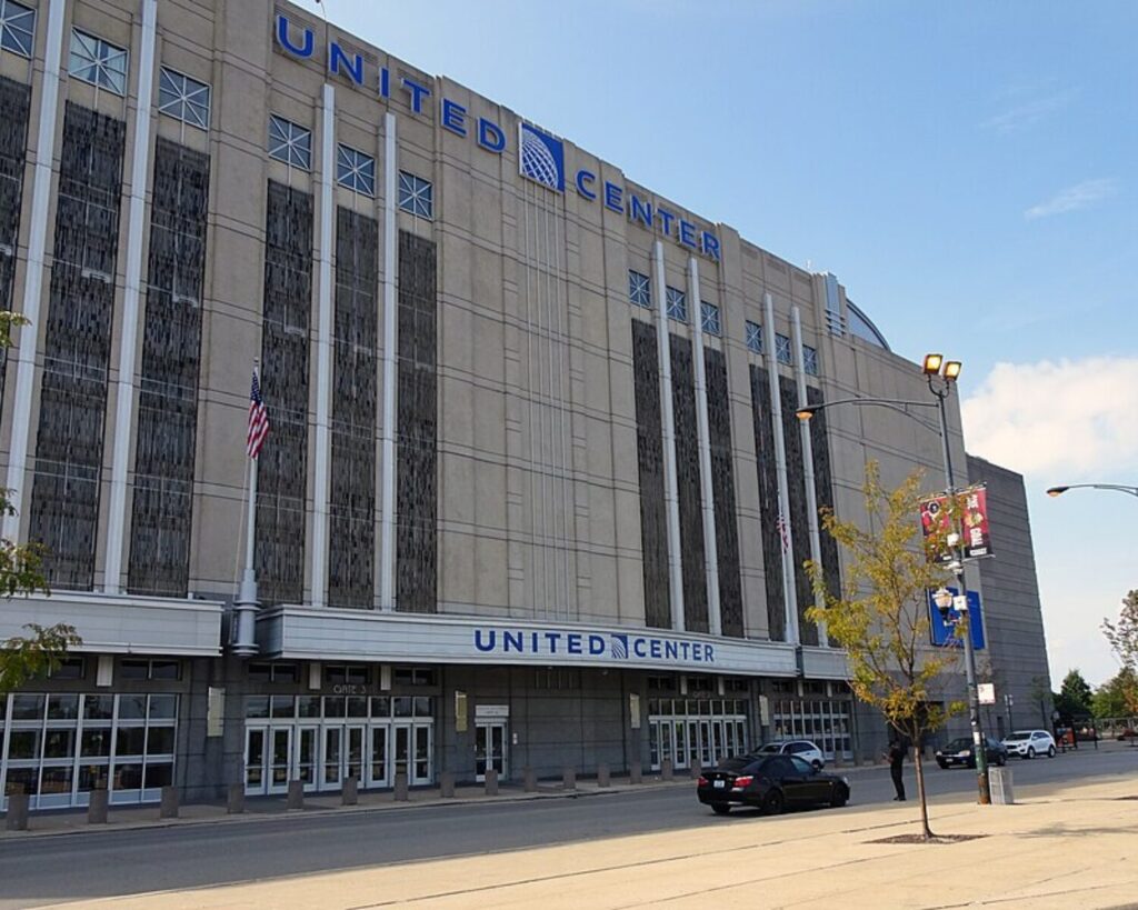 Exterior view of United Center arena with blue 'UNITED CENTER' sign, tall windows, and flagpoles along the entrance.