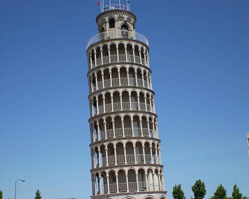 Leaning bell tower with multiple arched balconies against a clear blue sky.