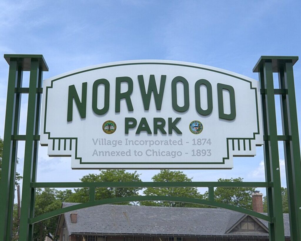 Sign at Norwood Park entrance reading 'Norwood Park' with 'Village Incorporated - 1874' and 'Annexed to Chicago - 1893' beneath; green decorative frame and blue sky behind.