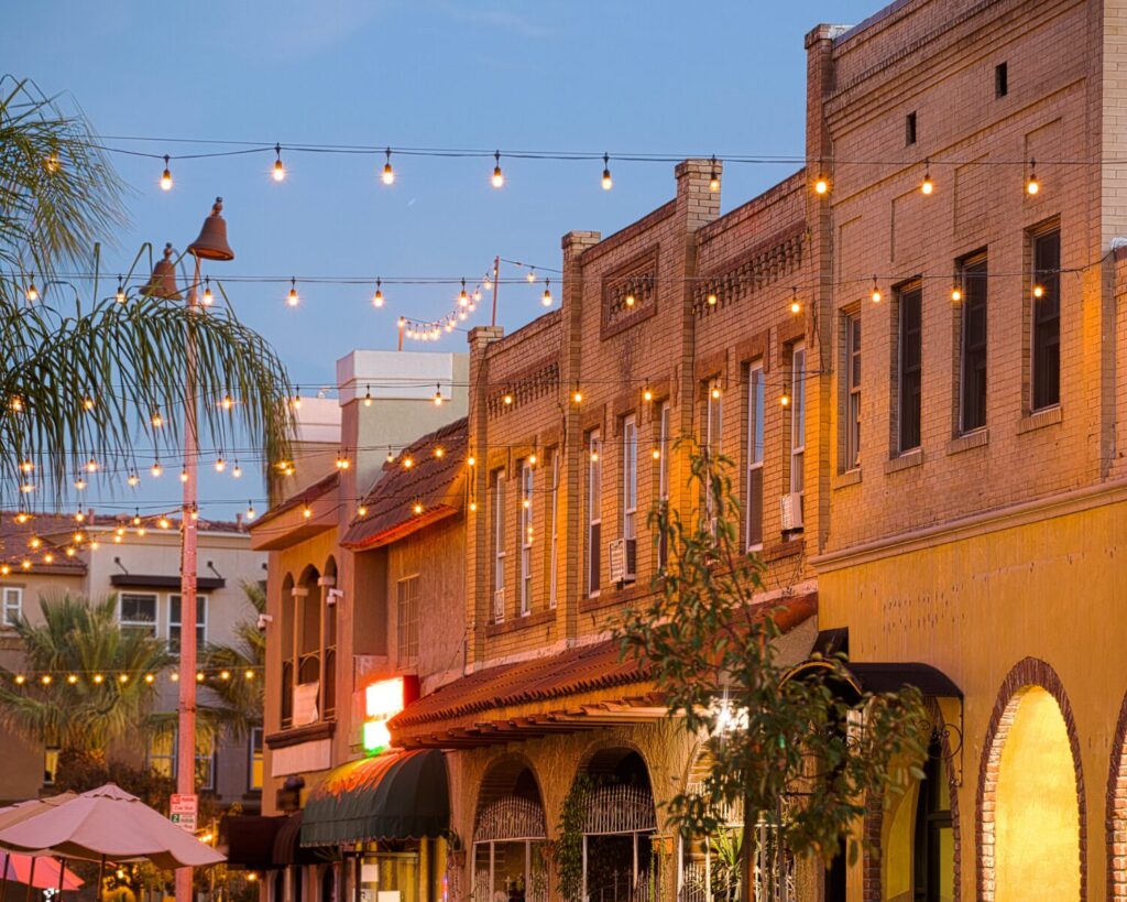 Placentia, California downtown street at dusk with brick buildings, palm trees, outdoor lights, and warm storefronts.