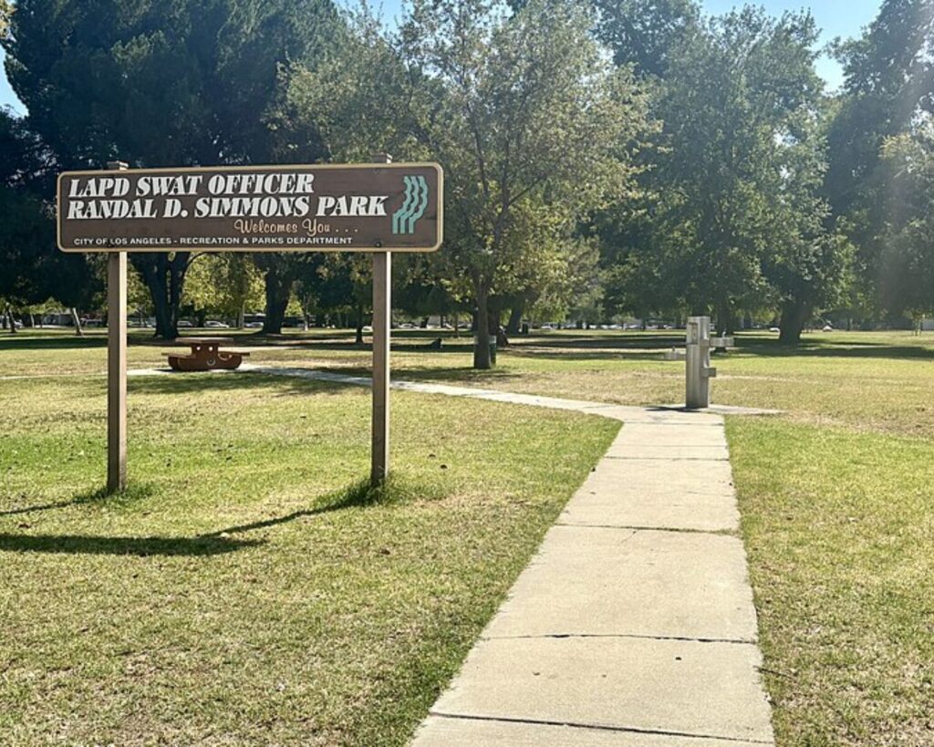 Randal D. Simmons Park in Reseda with park sign, grassy lawn, sidewalk, trees, and picnic area.