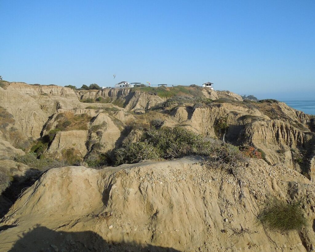 San Clemente State Beach bluffs with rugged coastal cliffs, dry vegetation, ocean view, and clear blue sky.