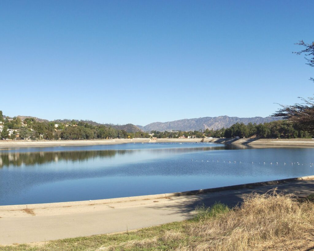 Silver Lake Reservoir with calm blue water, clear sky, hillside homes, trees, and distant mountains.
