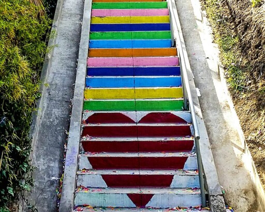 Colorful Micheltorena stairs with rainbow steps, red heart designs, surrounding greenery, and a narrow hillside walkway.