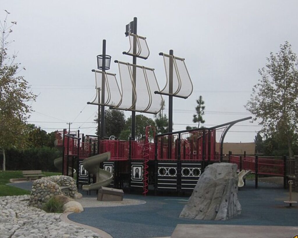 Pirate ship-themed playground at Harry Dotson Park with slides, climbing rocks, trees, and outdoor play area.