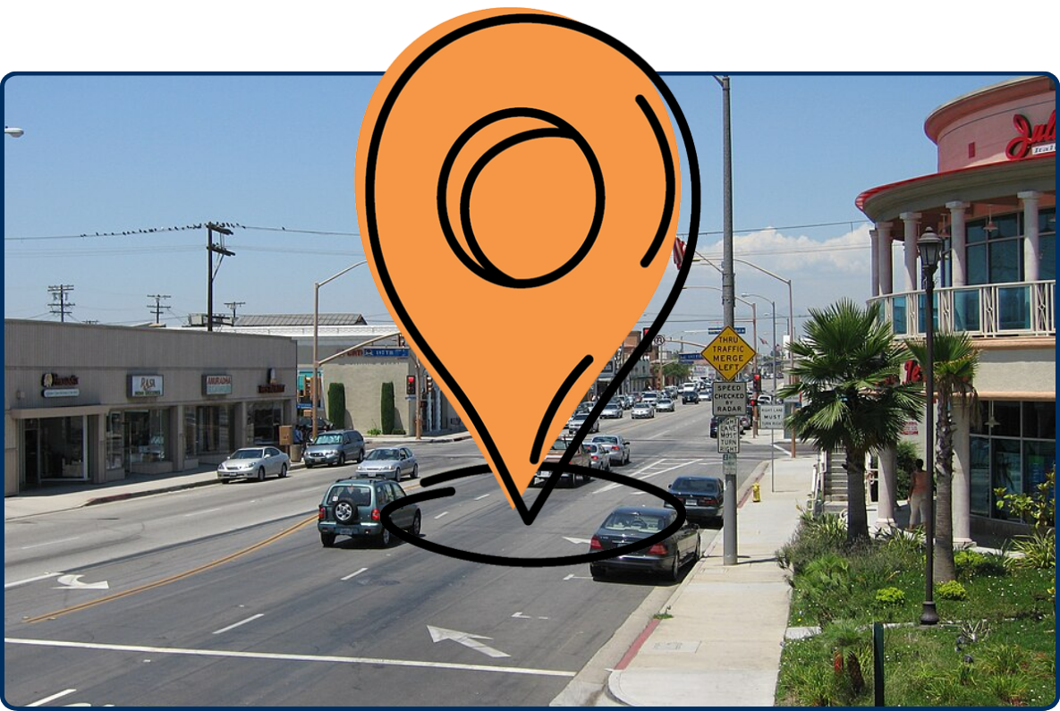 Busy commercial street in Artesia, California, with cars, shops, palm trees, and traffic lights under a clear blue sky.